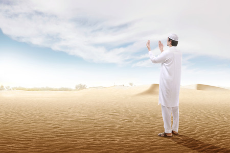 Rear view of asian muslim man raised hands and praying on the sand dune with blue sky backgroundの写真素材