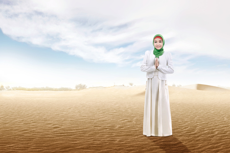 Smiling asian muslim woman in veil praying on the sand dune with blue sky backgroundの写真素材