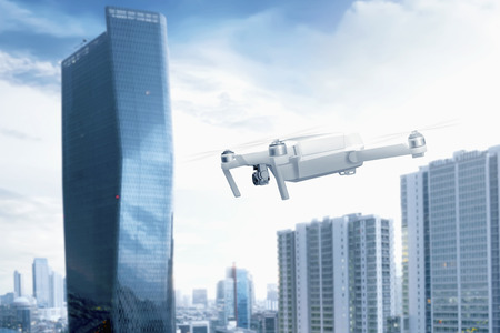 White drone with camera flying over the city with skyscrapers and blue sky backgroundの写真素材