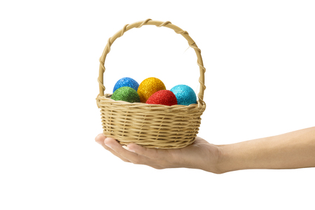Human hand holding wooden basket with colorful easter eggs isolated over white background. Happy Easterの写真素材