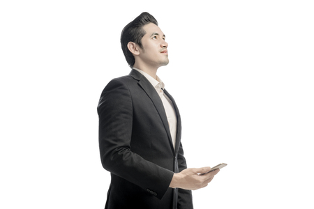 Portrait of asian businessman looking up and holding the mobile phone posing isolated over white backgroundの写真素材