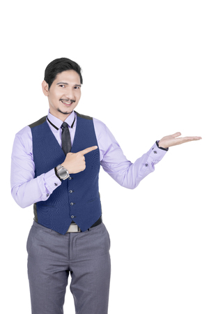 Young asian businessman pointing his open palm posing isolated over white backgroundの写真素材