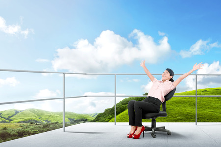 Pretty asian business woman sitting on the chair and relaxing on the terrace with green landscapes view and blue sky backgroundの写真素材