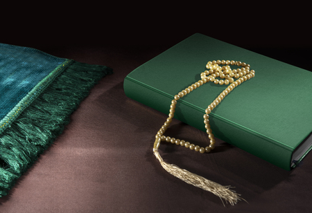 Quran and prayer beads with prayer mat on the floor over black backgroundの写真素材