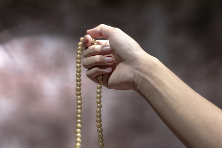 Muslim hands praying with prayer beads over blurry backgroundの写真素材