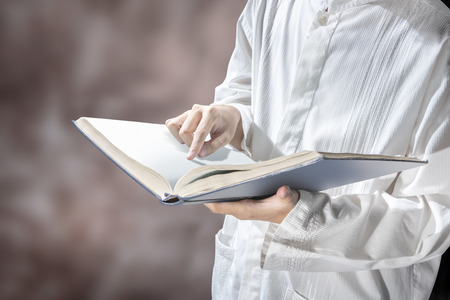 Muslim man standing while reading the quran on his hands over blurry backgroundの写真素材