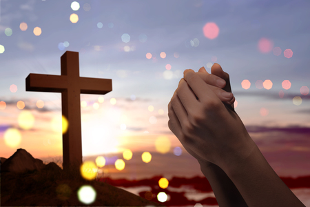 Christian cross and male hands with praying position over sunset backgroundの写真素材