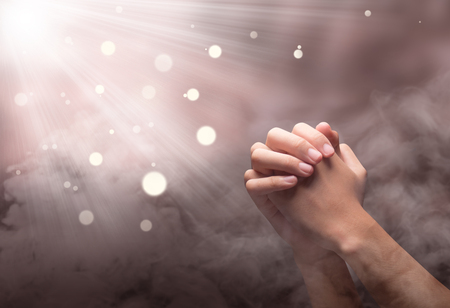 Male hands in praying position with ray over blurry background