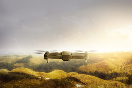 White drone with camera flying above green hills and trees with sunlight backgroundの写真素材