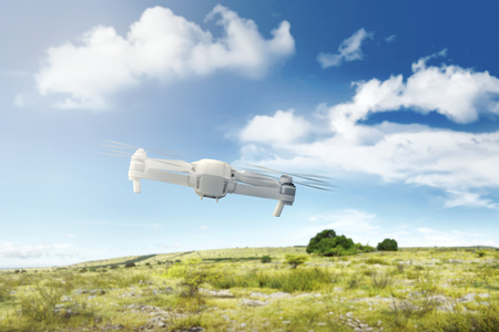 White drone with camera flying above the field with green grass and trees with blue sky backgroundの写真素材