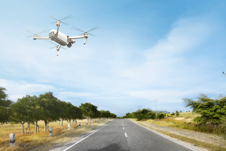White drone with camera flying above the street with trees and grass over blue sky backgroundの写真素材