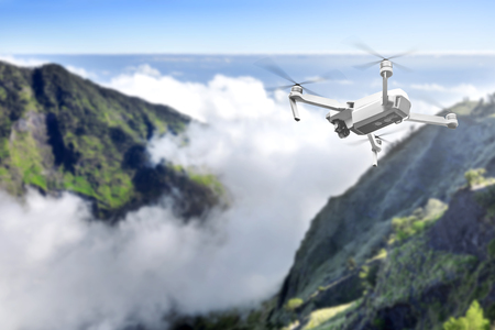 White drone with camera flying above the top of mountain with cloudscapes and blue sky backgroundの写真素材
