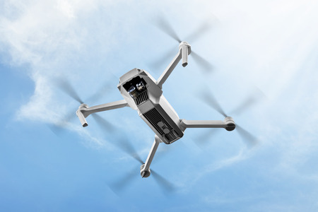 White drone with camera flying in the air over blue sky background