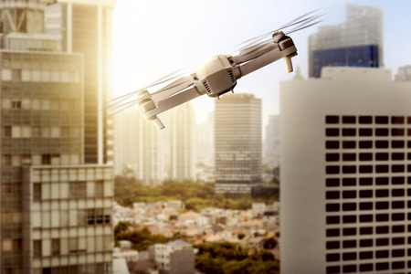 White drone with camera flying above modern city with skyscrapers and sunset view backgroundの写真素材