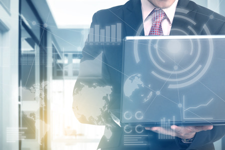 Businessman holding laptop with his hand with virtual screen which display the interface of financial chart and world maps. Digital technology conceptの写真素材