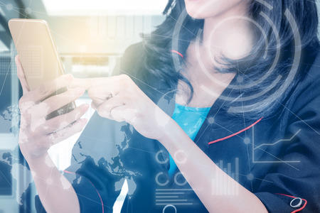 Business woman using mobile phone with virtual screen which display the interface of financial chart and world maps. Digital technology conceptの写真素材