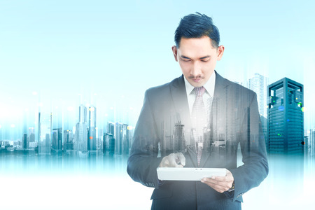 Double exposure of modern city and handsome asian businessman using digital tablet in his hand. Future technology conceptの写真素材