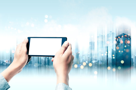 Businessman holding the mobile phone with white blank screen for copyspace with modern city background. Future technology conceptの写真素材