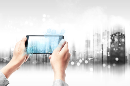 Businessman holding the mobile phone and display the interface a modern city with blurry modern city background. Future technology conceptの写真素材
