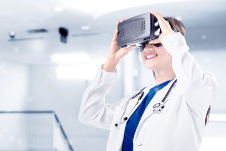 Asian female doctor in white coat and stethoscope using virtual reality device on the hospital. Augmented reality technologyの写真素材