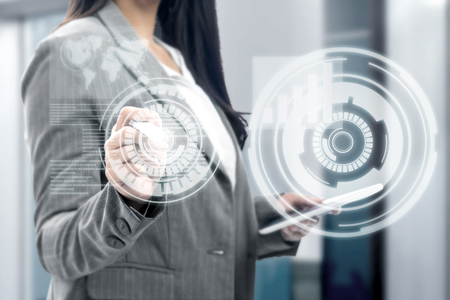Business woman holding digital tablet and drawing with marker on virtual screen which display the interface of financial chart and world maps. Digital technology conceptの写真素材