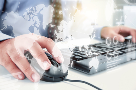 Businessman working with keyboard and mouse on the desk with display interface of world map, chart and graphs. Digital technology conceptの写真素材