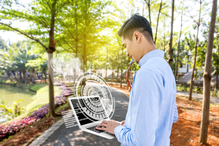 Rear view of asian businessman looking at the laptop with virtual screen which display the interface of world map and binary code on the park. Digital technology conceptの写真素材