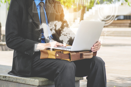 Businessman sitting and working with laptop with virtual screen which display the interface of financial chart, world maps and binary code. Digital technology conceptの写真素材