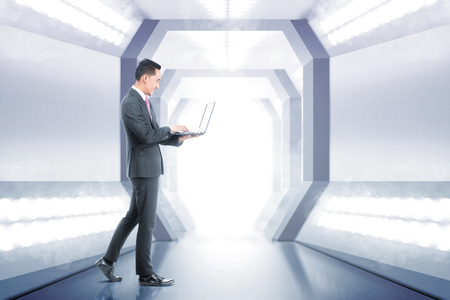 Side view of asian asian businessman holding laptop with his hand while walking on the office corridor. Future technology conceptの写真素材