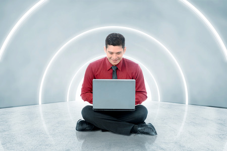 Smiling asian businessman sitting and using laptop on the office corridor. Future technology conceptの写真素材