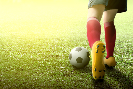 Rear view of football player woman in orange jersey kicking the ball on the green fieldの写真素材