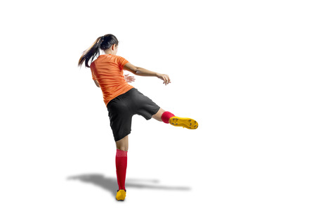 Rear view of asian football player woman in orange jersey with kicking the ball position isolated over white backgroundの写真素材
