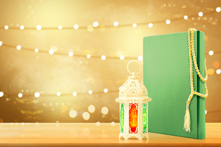 Quran with prayer beads and arabic lamp with beautiful light on wooden table with blurry lights backgroundの写真素材