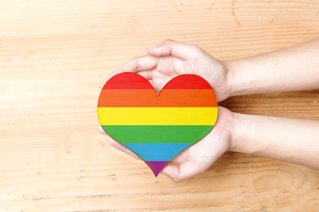 Human hands holding heart with rainbow flag over wooden table background. LGBT conceptの写真素材