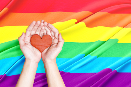 Human hands holding heart with rainbow flag background. LGBT conceptの写真素材