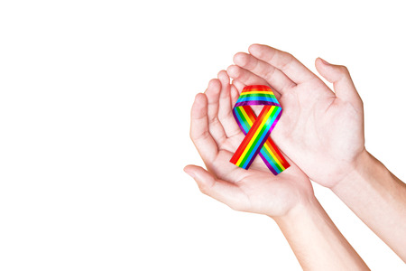 Human hands holding ribbon with rainbow flag as a symbol of LGBT isolated over white backgroundの写真素材