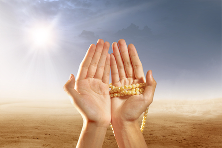Muslim hands praying with prayer beads on desert with sun rays and dark sky backgroundの写真素材