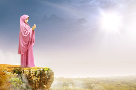 Asian muslim woman in veil raised hands and praying on the edge of the cliff with sunlight and landscapes backgroundの写真素材