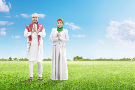 Asian muslim man with cap and muslim woman with veil praying together on the green grass field with blue sky backgroundの写真素材