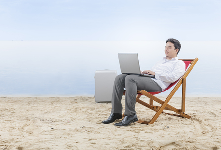 Asian businessman working with laptop sitting in the beach chair on beach. Summer vacationの写真素材