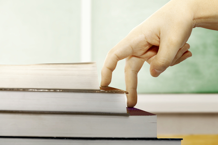 Close up view of fingers hand climb the book steps on wooden table with chalkboard background. Back to School conceptの写真素材