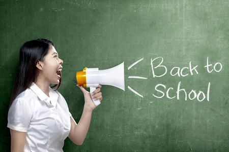 Asian teacher woman using megaphone to notify for go back to school with chalkboard background. Back to School conceptの写真素材