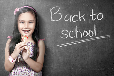 Asian student girl standing and holding candy with blackboard background. Back to School conceptの写真素材
