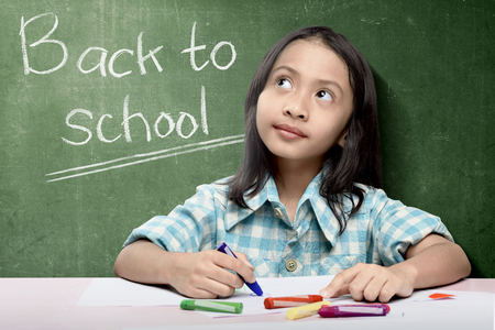 Asian student girl drawing on white paper with colorful crayons over chalkboard background. Back to School conceptの写真素材