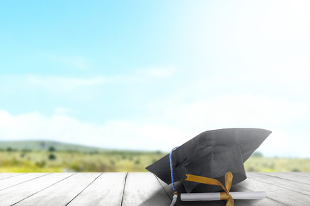 Mortarboard hat and diploma on wooden table with landscapes and blue sky background. Graduation conceptの写真素材