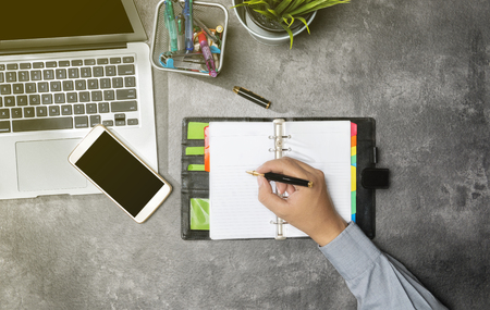 Top view of businessman writing in notebook with laptop, potted plant, mobile phone and business accessories on the officeの写真素材