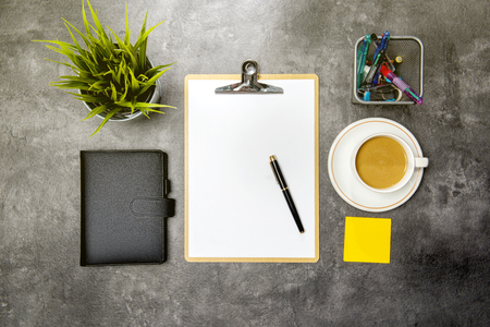 Top view of business desk with potted plant, clipboard, notebook, coffee, notes paper and business accessories on the officeの写真素材