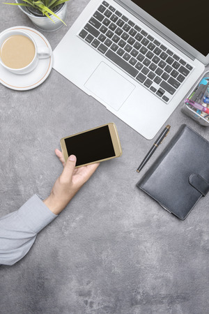 Top view of businessman using mobile phone with laptop, coffee, potted plant, notebook and business accessories on the office deskの写真素材