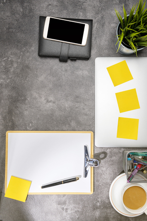 Top view of business desk with laptop, mobile phone, coffee, potted plant, notebook, notes paper, clipboard and business accessories on the officeの写真素材