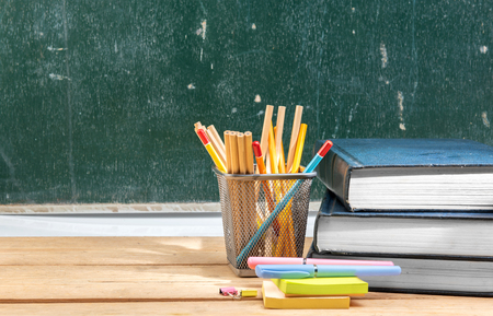 Pile of books with notes paper and pen with pencils in basket container on wooden table with chalkboard background. Back to School conceptの写真素材